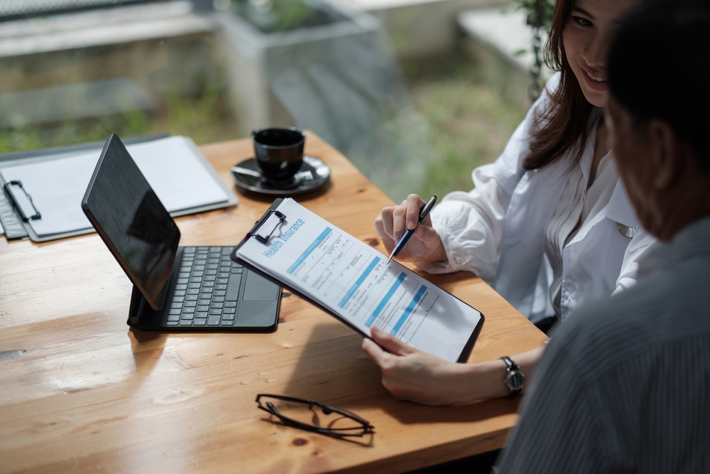 Female health insurance broker presenting insurance benefits to businessman fills out insurance policy