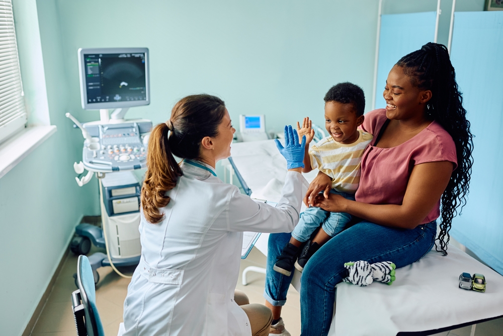 Happy young boy giving high five to his pediatrician after medical examination at doctor’s office